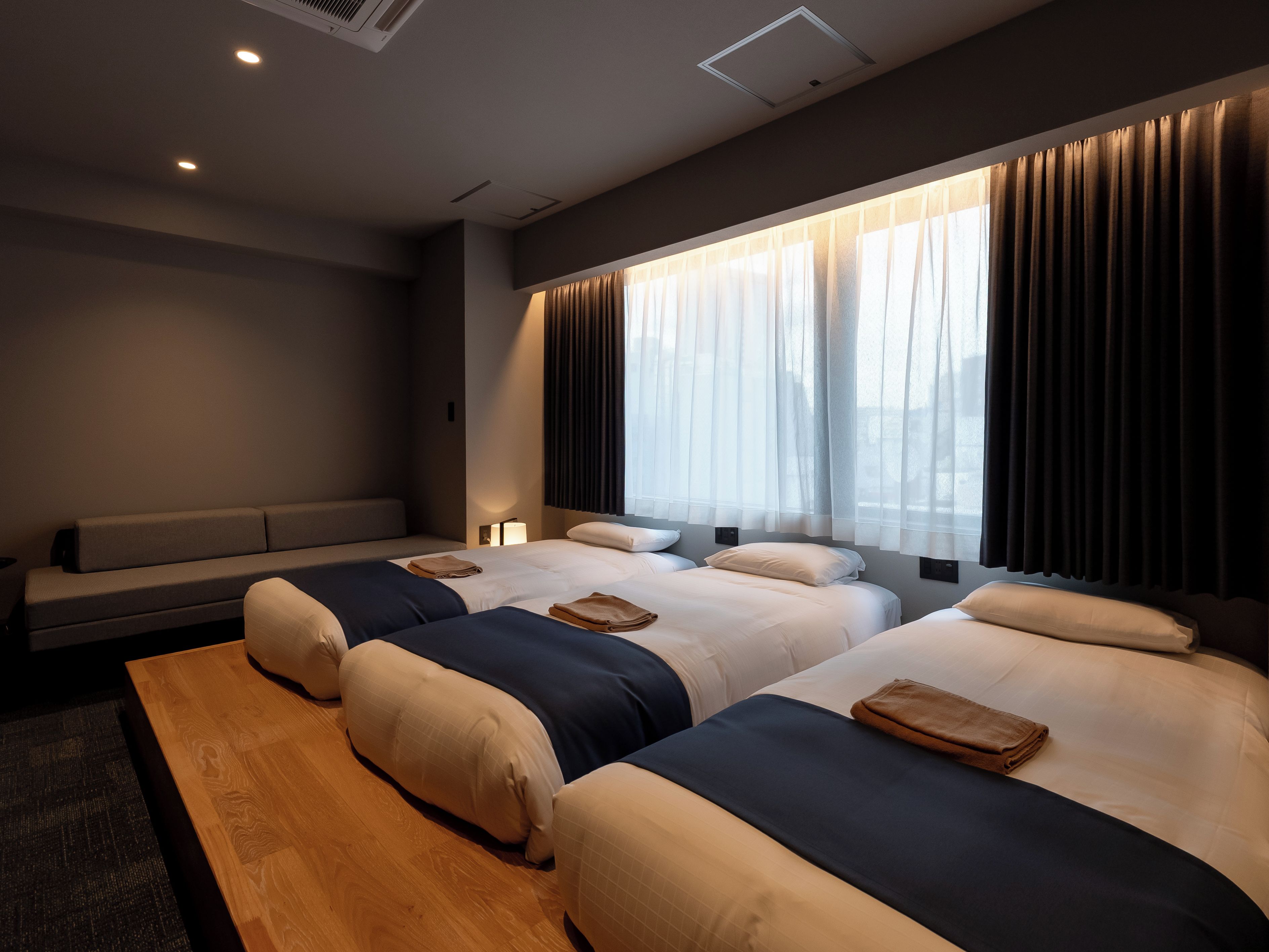 A hotel room with three beds, a bench, and a wooden floor.