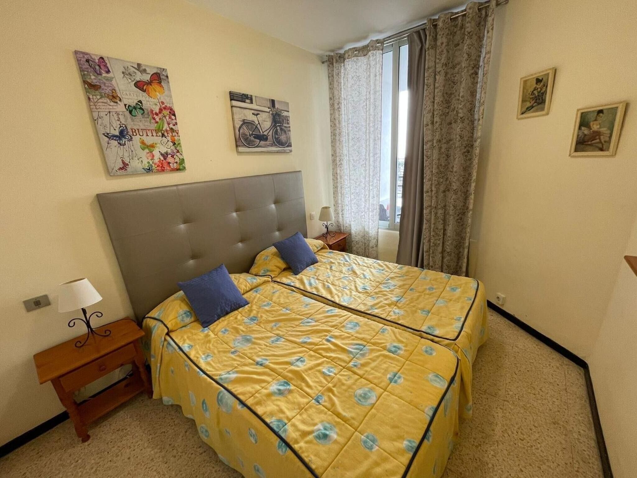 A double bed with a floral bedspread, a nightstand with a lamp, and a window with curtains.