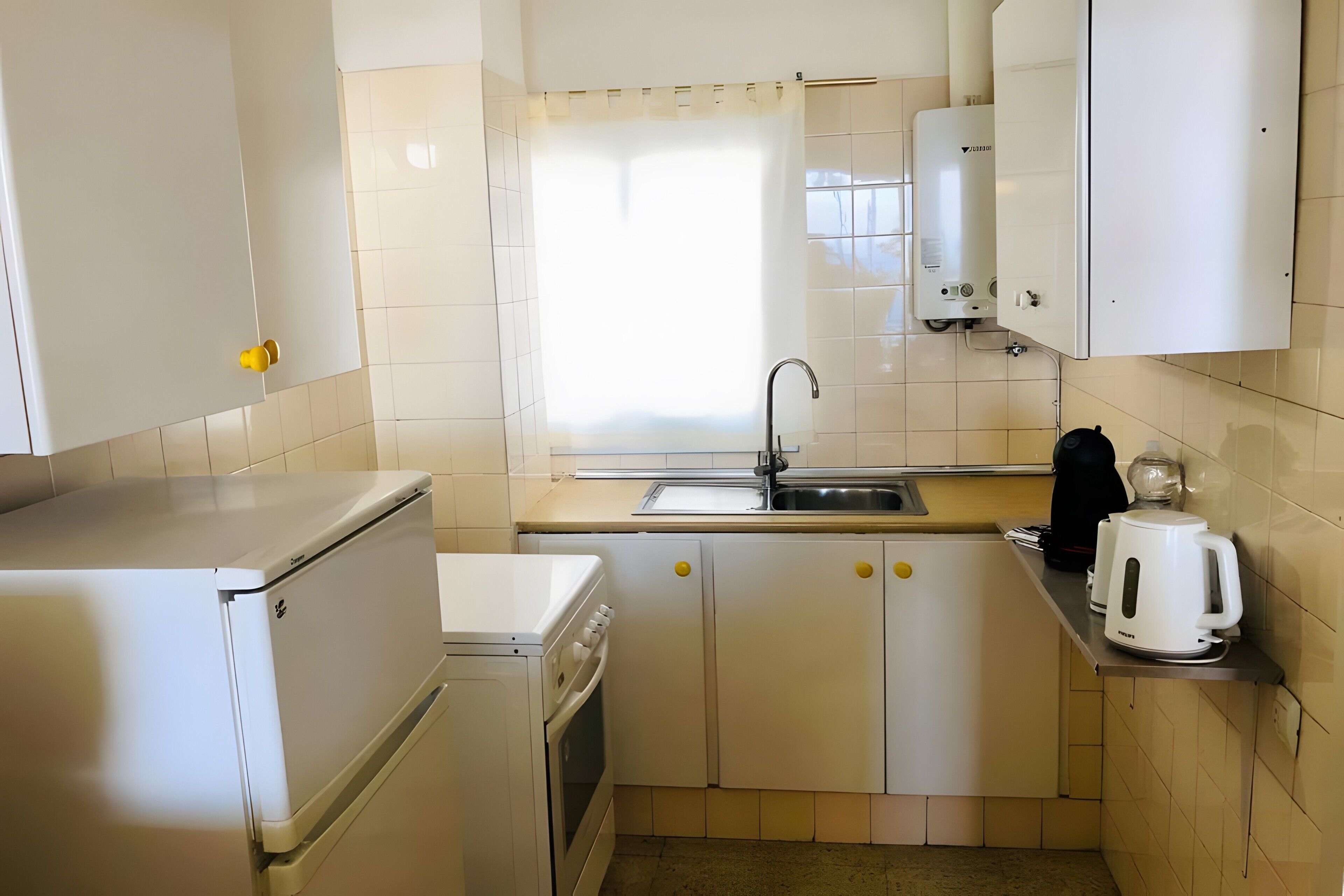 A compact kitchen with white appliances, a sink, and a window.