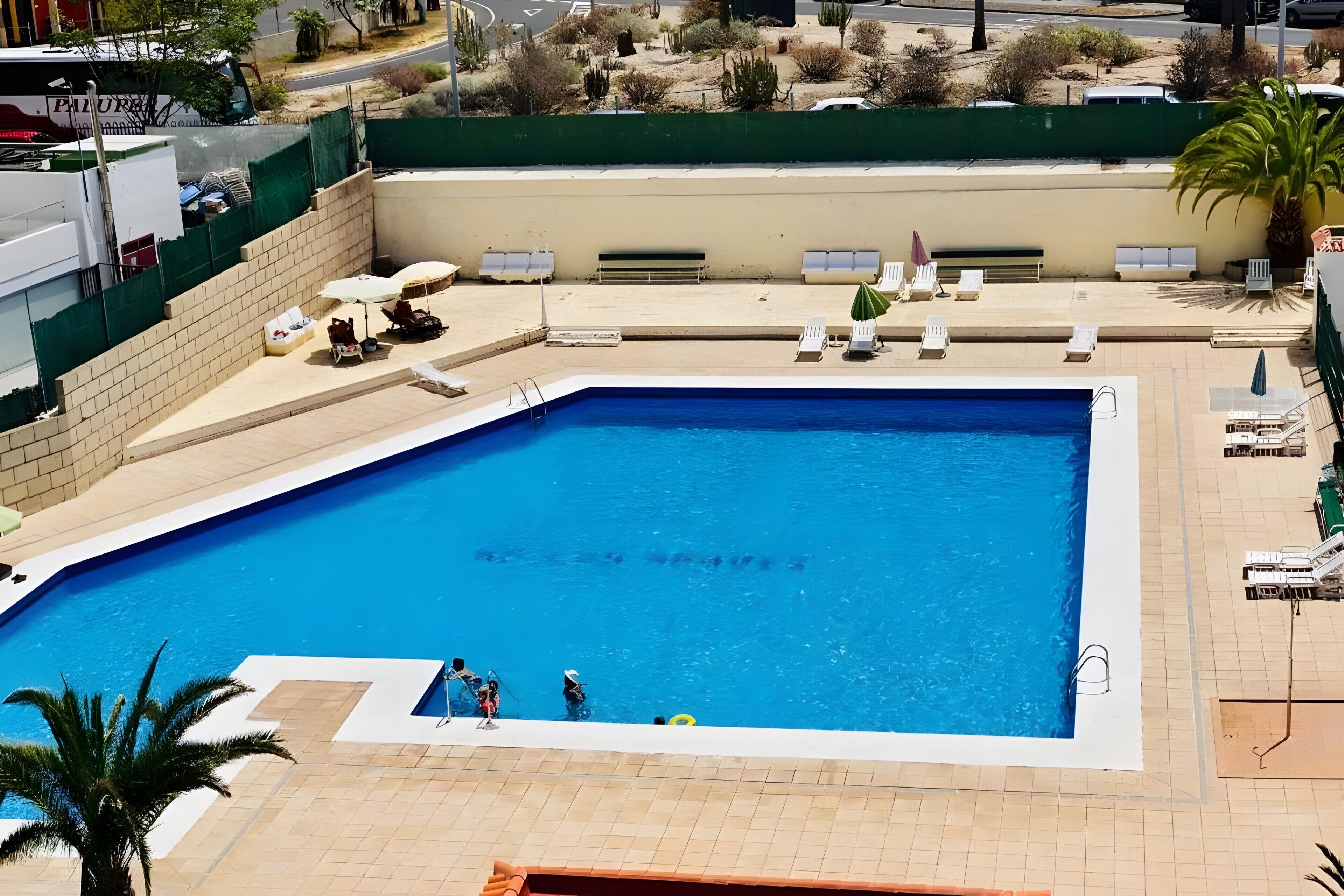 A rectangular swimming pool with a tiled deck surrounding it, equipped with lounge chairs and umbrellas.
