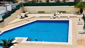 A rectangular swimming pool with a tiled deck surrounding it, equipped with lounge chairs and umbrellas.