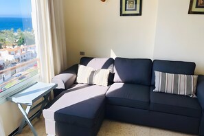 Ein modernes Wohnzimmer mit einem dunkelgrauen Sofa, einem kleinen Beistelltisch und Meerblick durch ein großes Fenster.