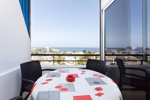 Een balkon met een tafel en stoelen, met uitzicht op een stadsbeeld en de zee.