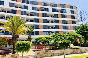 Ein mehrstöckiges Hotel mit Balkonen, einer Palme und einem angelegten Garten.