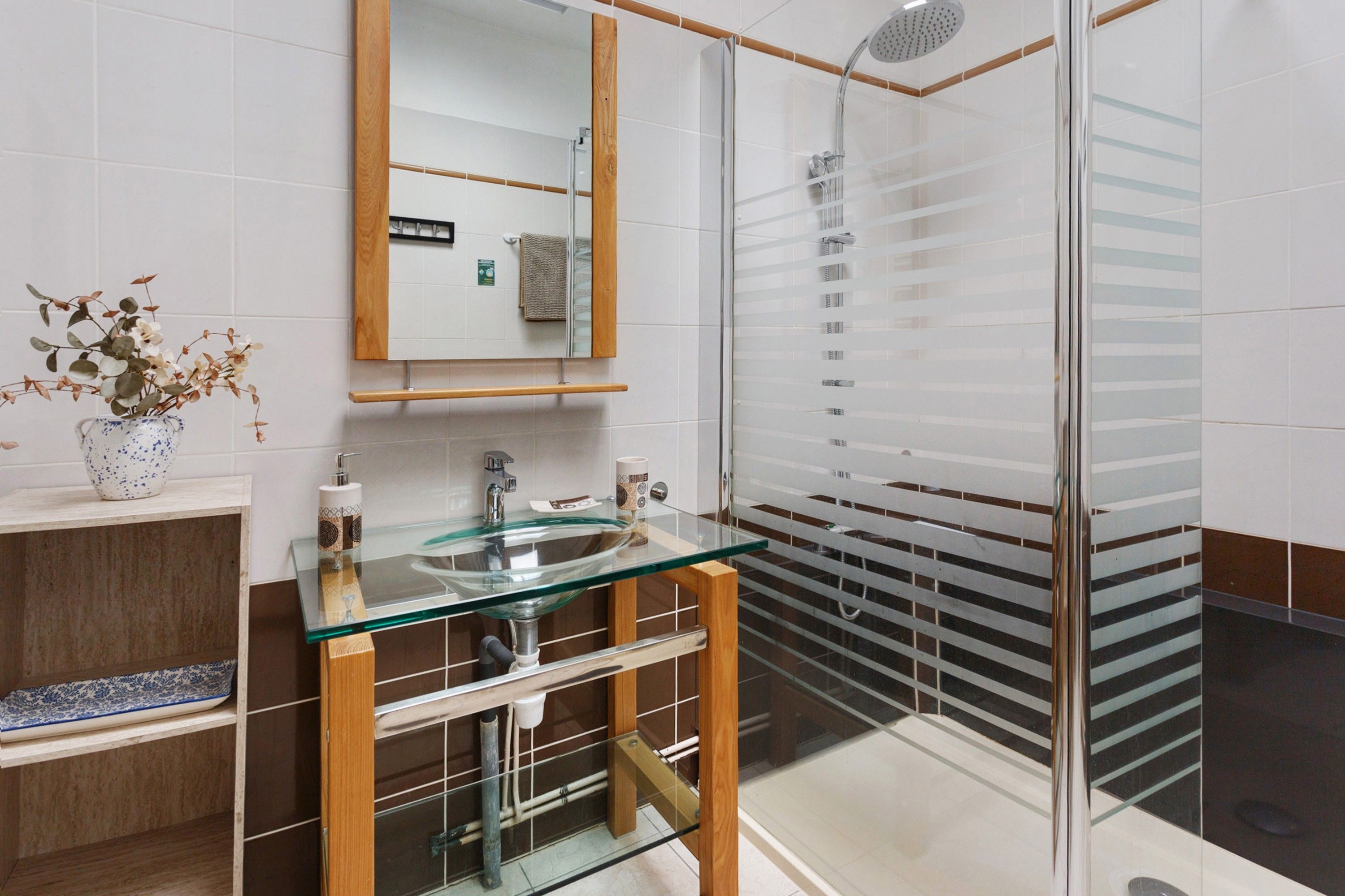 A modern bathroom with a glass sink, wooden vanity, and a glass shower enclosure.