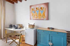 A compact kitchen with a coffee maker, a refrigerator, and a teal cabinet.