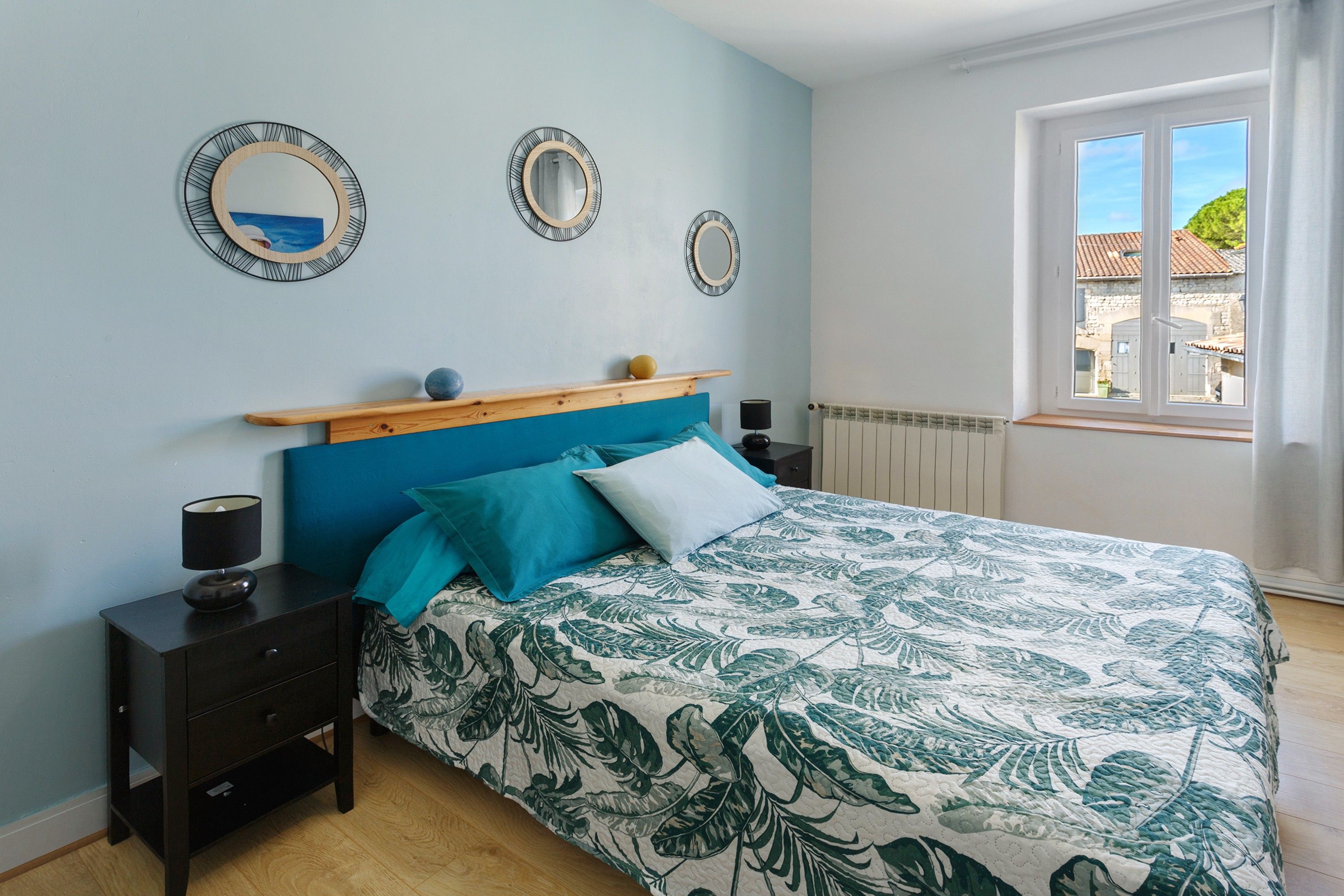Een slaapkamer met een bed, nachtkastjes, een raam en spiegels aan de muur.