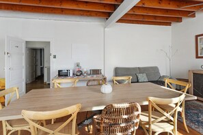 Ein Essbereich mit einem Holztisch, Korbstühlen und einer Küche im Hintergrund.