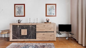 A room with a wooden cabinet, two framed artworks on the wall, a television, and a patterned rug.