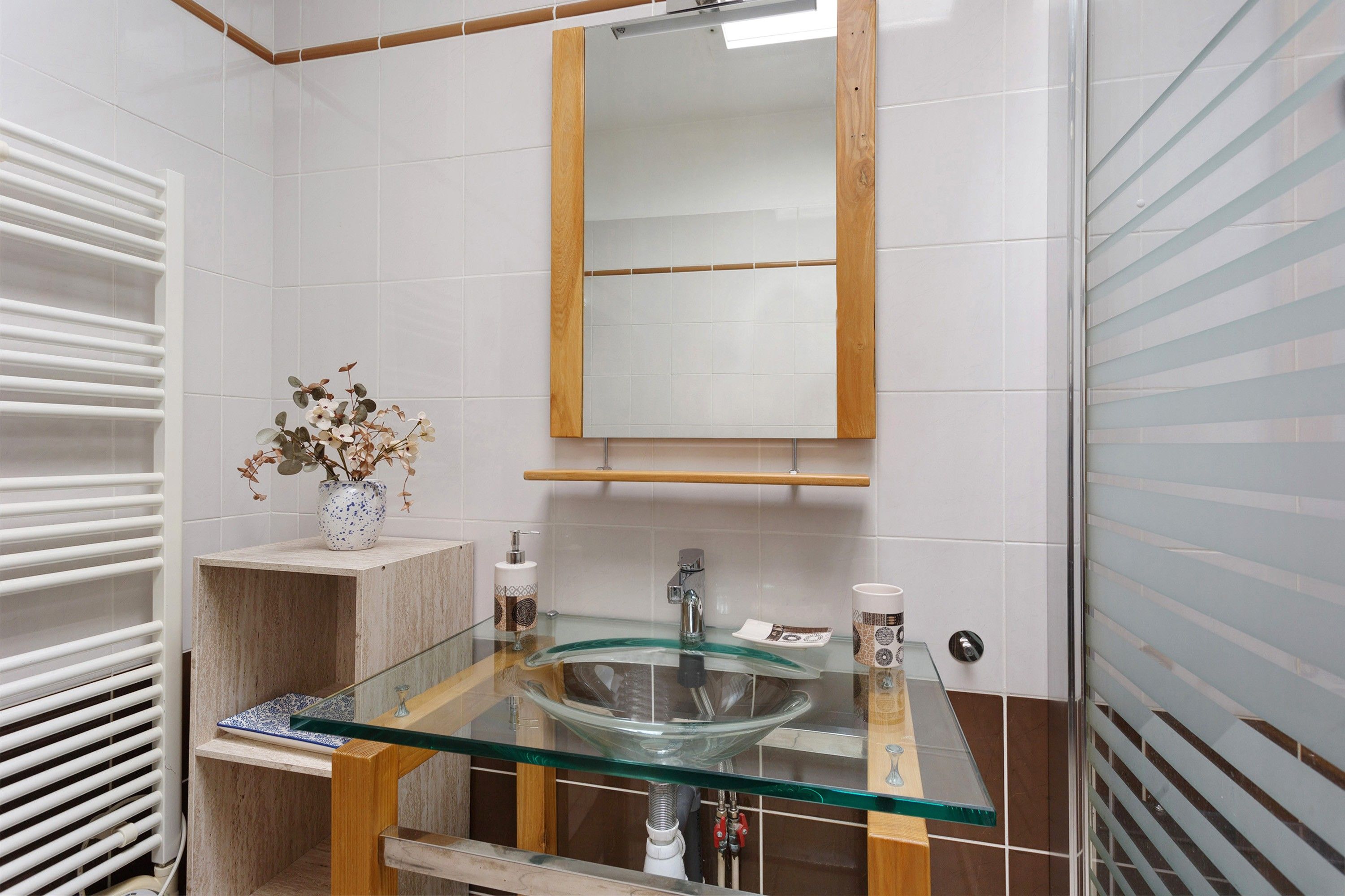Ein Badezimmer mit einem Glastischwaschbecken, einem Holzwaschtisch, einem Spiegel und einem Handtuchhalter.
