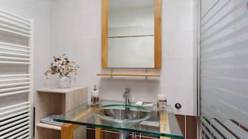 Ein Badezimmer mit einem Glastischwaschbecken, einem Holzwaschtisch, einem Spiegel und einem Handtuchhalter.