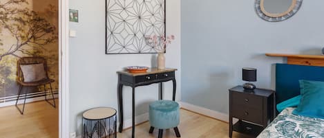 A room with a bed, a small table with a vase, a chair, and a wall-mounted mirror.