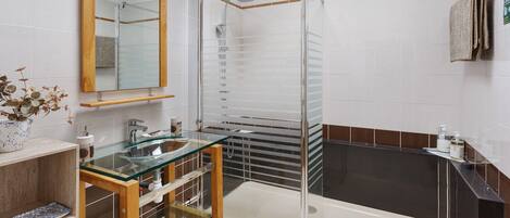 Un baño moderno con ducha envuelta en vidrio, tocador de madera con cubierta de cristal y un espejo grande.