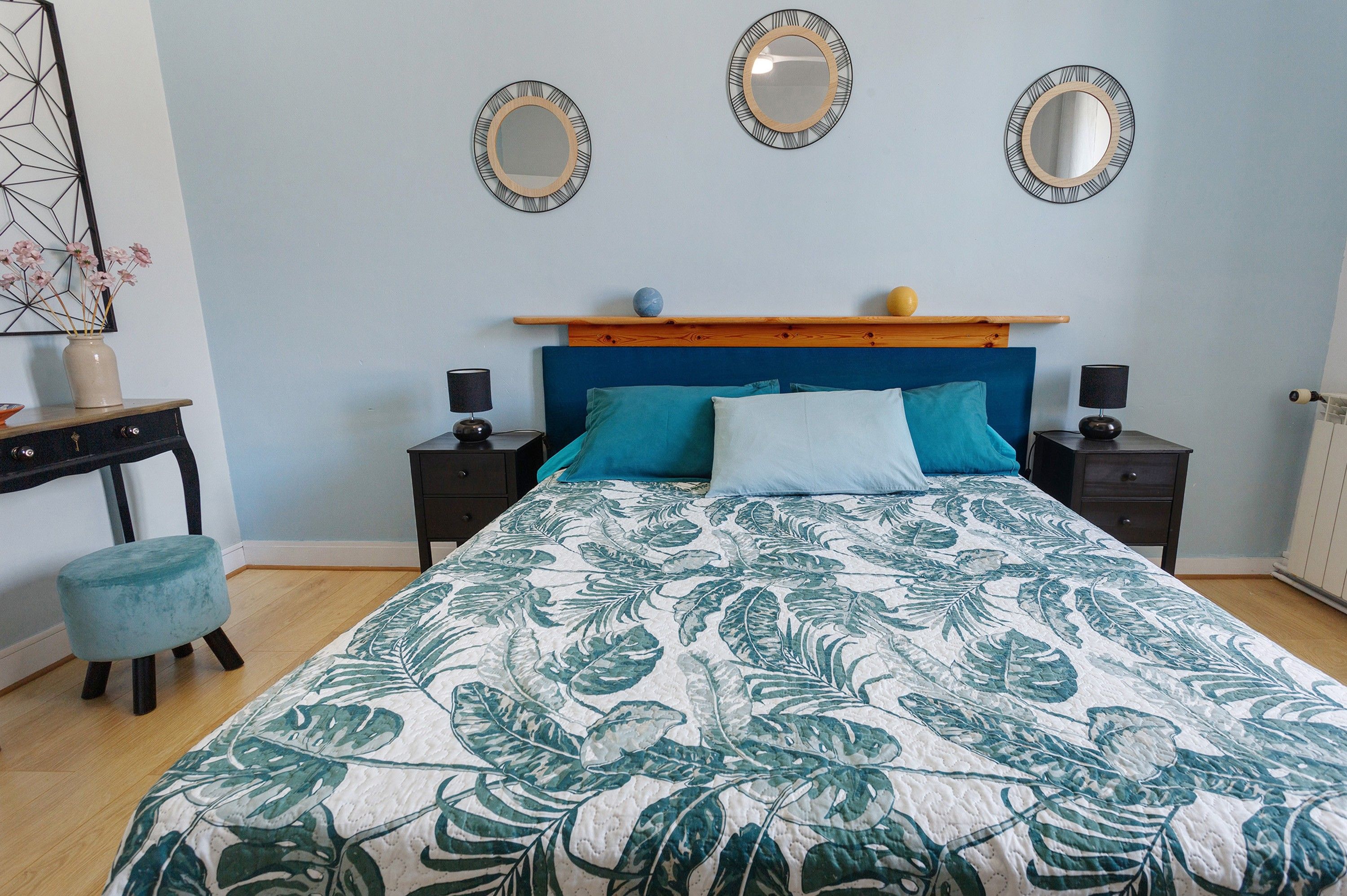 A bedroom with a bed, two nightstands, a dresser, and three wall mirrors.