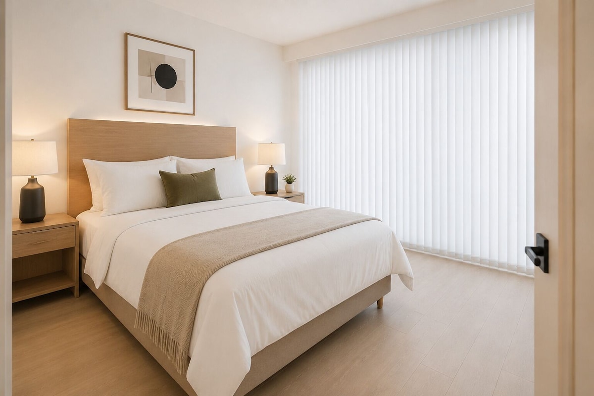 Ein Hotelzimmer mit einem großen Bett, zwei Nachttischen mit Lampen, einer Kopfteil und einem gerahmten Bild an der Wand sowie einem großen Fenster mit Jalousien.