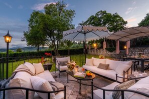 An outdoor patio with a covered seating area, a table with books and fruit, and a view of the landscape. - Refined And Luxurious Villa In the Outskirts Of Lucca (Lucca)