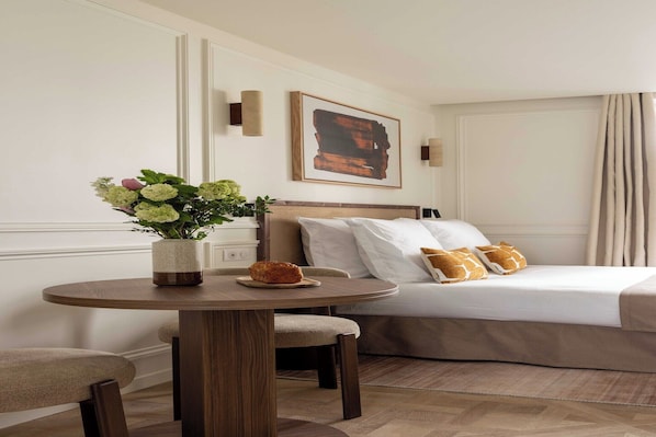 Een hotelkamer met een bed, een ronde houten tafel met een bloevas, en een schilderij aan de muur.