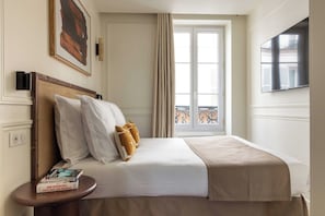 Een hotelkamer met een bed, een nachtkastje, een raam met gordijnen, een tv aan de muur en een schilderij.