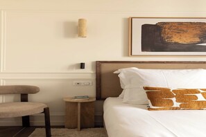 Een hotelkamer met een bed, een stoel, een klein tafeltje en een wandlamp.
