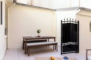 Een klein terras met een houten tafel en bankje, een zwart hek en een betegelde vloer.