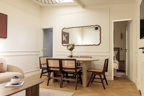 Een eethoek met een ronde tafel, zes stoelen, een vaas met bloemen en een grote spiegel aan de muur.