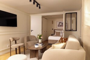Een moderne woonkamer met een flatscreen televisie, een bank, twee fauteuils, een salontafel en een bed op de achtergrond.