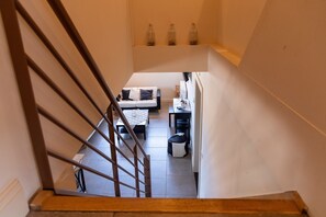 Una escalera conduce a un área de estar con un sofá, una mesa de centro y una mesita con objetos decorativos.