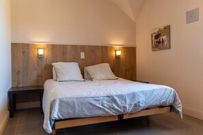 Un dormitorio con cabecera de madera, dos lámparas de noche, una cama con ropa de cama estampada y un cuadro colgado en la pared.