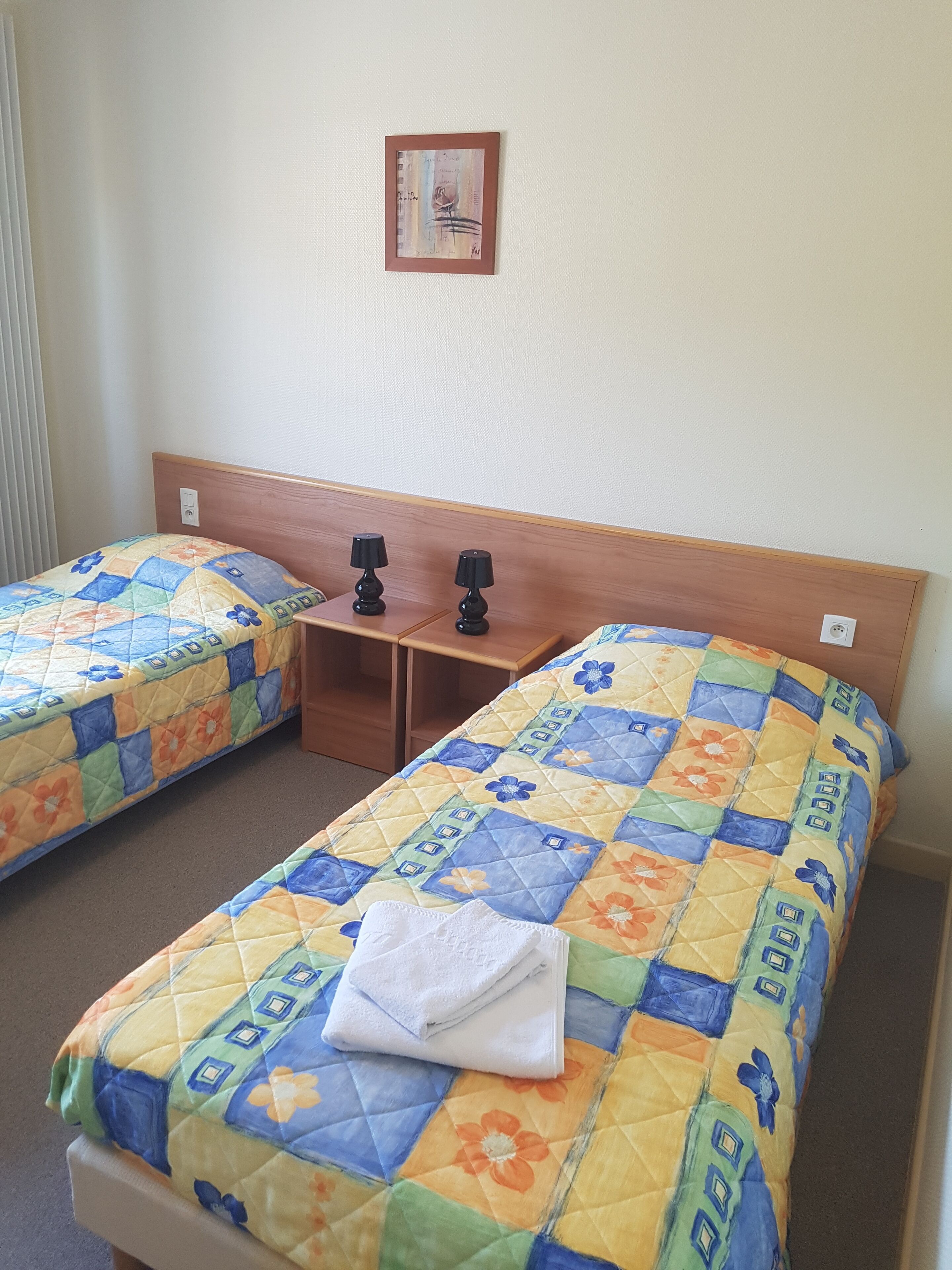 Une chambre d’hôtel avec deux lits simples, chacun doté d’une couvre-lit matelassé et d’une petite table de chevet avec une lampe.