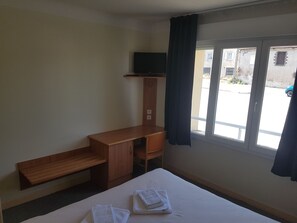 Een hotelkamer met een bed, een houten bureau, een televisie op een plank en een raam met gordijnen.