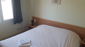 A hotel room with a large bed, a bedside table with a lamp, a window with curtains, and a framed picture on the wall.