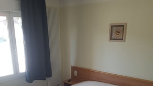 A hotel room with a large bed, a bedside table, a window with curtains, and a framed picture on the wall.