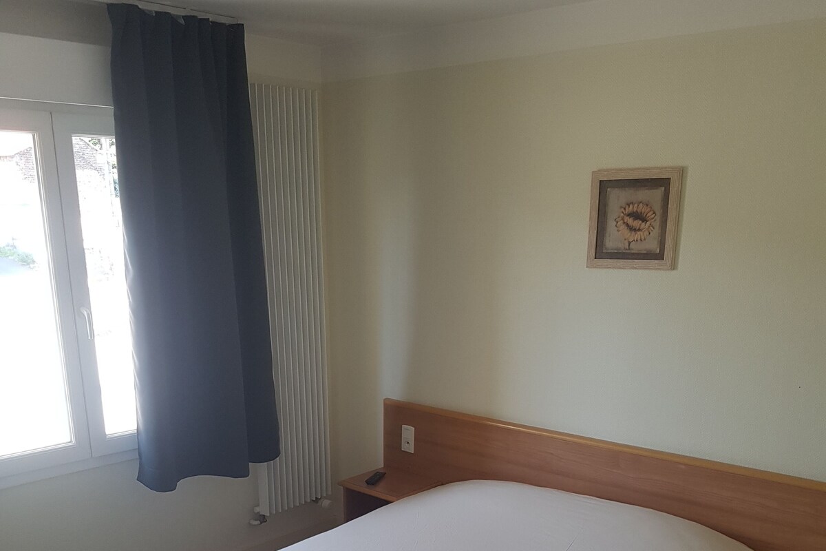 Een hotelkamer met een groot bed, een nachtkastje, een raam met gordijnen en een lijst met een foto aan de muur.