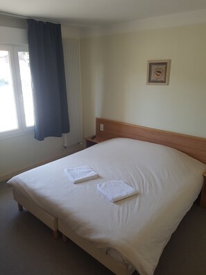 Een hotelkamer met een groot bed, een nachtkastje, een raam met gordijnen en een lijst met een foto aan de muur.