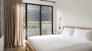 Une chambre d’hôtel avec un grand lit, une fenêtre avec des stores, un rideau et une table de chevet avec une lampe.