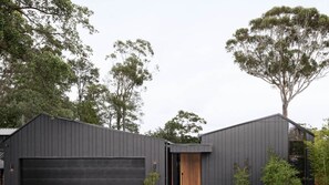 A modern building with a dark exterior, a garage door, and a wooden door. - Inkwood House | Luxury Stay in Mollymook with mineral pool and private sauna (Mollymook)