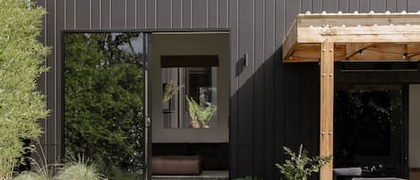 Un bâtiment moderne doté d'une grande entrée avec une porte-fenêtre coulissante, d'un espace extérieur aménagé avec des sièges et d'un jardin bien entretenu.
