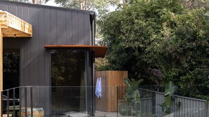 Ein modernes Gebäude mit dunkler Fassade, einer Holzterrasse und einem Glastür-Eingang.
