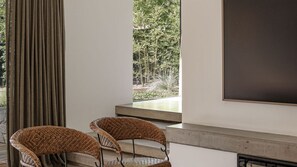 Ein modernes Zimmer mit großem Fenster, zwei Korbstühlen, einer dunklen Wand und einem Kamin.
