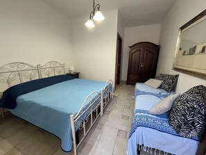 Une chambre avec un grand lit, un plus petit lit, une armoire et un miroir au mur.
