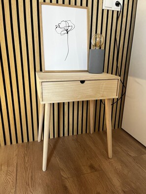 Ein Holztisch mit einer Schublade, eine gerahmte Schwarz-Weiß-Zeichnung einer Blume und eine Glasvase mit einer Zwiebel obenauf.