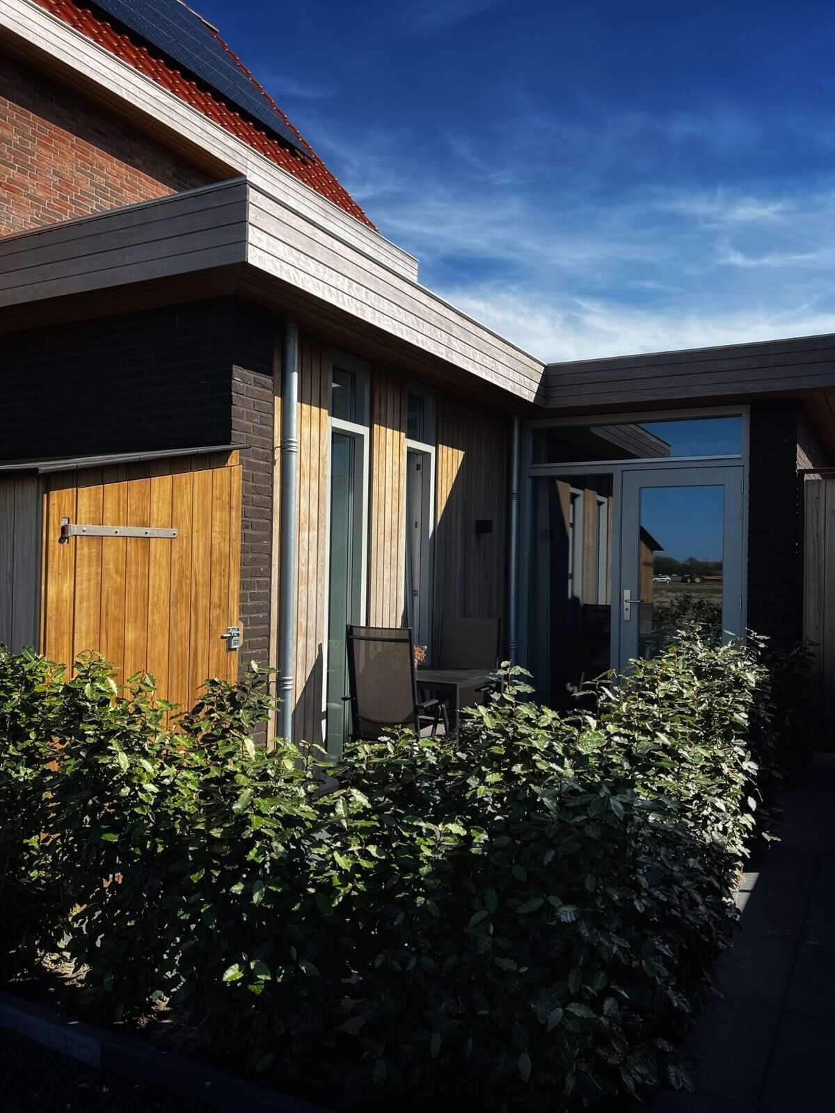 Een modern huis met een houten gevel, een garagepoort en een terras met een tafel en stoel.