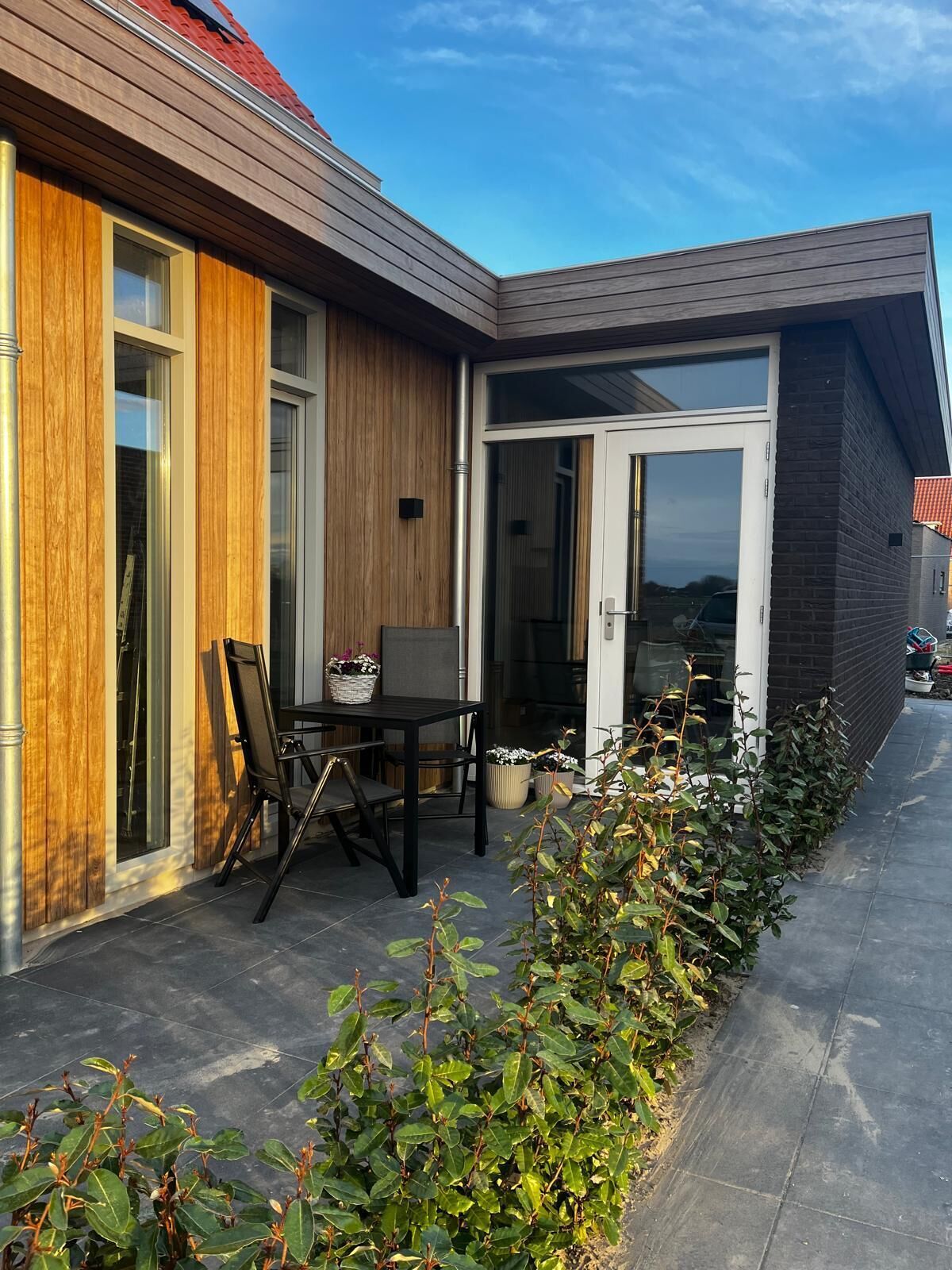 Ein modernes Haus mit Terrasse, einem Esstisch mit Stühlen und einem Garten.
