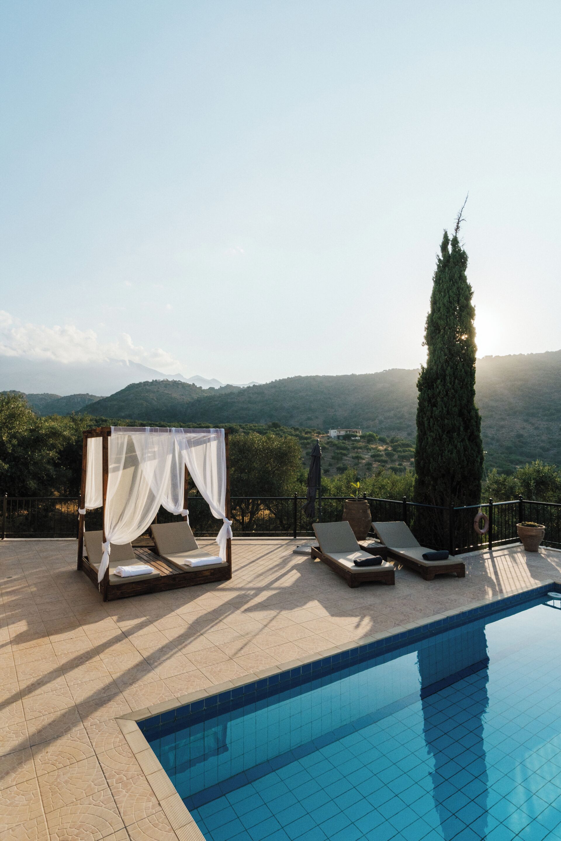 A poolside area with a bed, lounge chairs, and a view of the mountains.