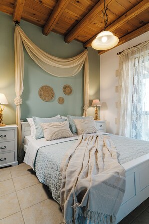 A bedroom with a bed, bedside tables, a hanging light fixture, and a window with curtains. - Villa Elia Provarma by Your Villa (Stilos)