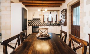 A kitchen with a wooden table, chairs, and a checkered backsplash. - Villa Elia Provarma by Your Villa (Stilos)