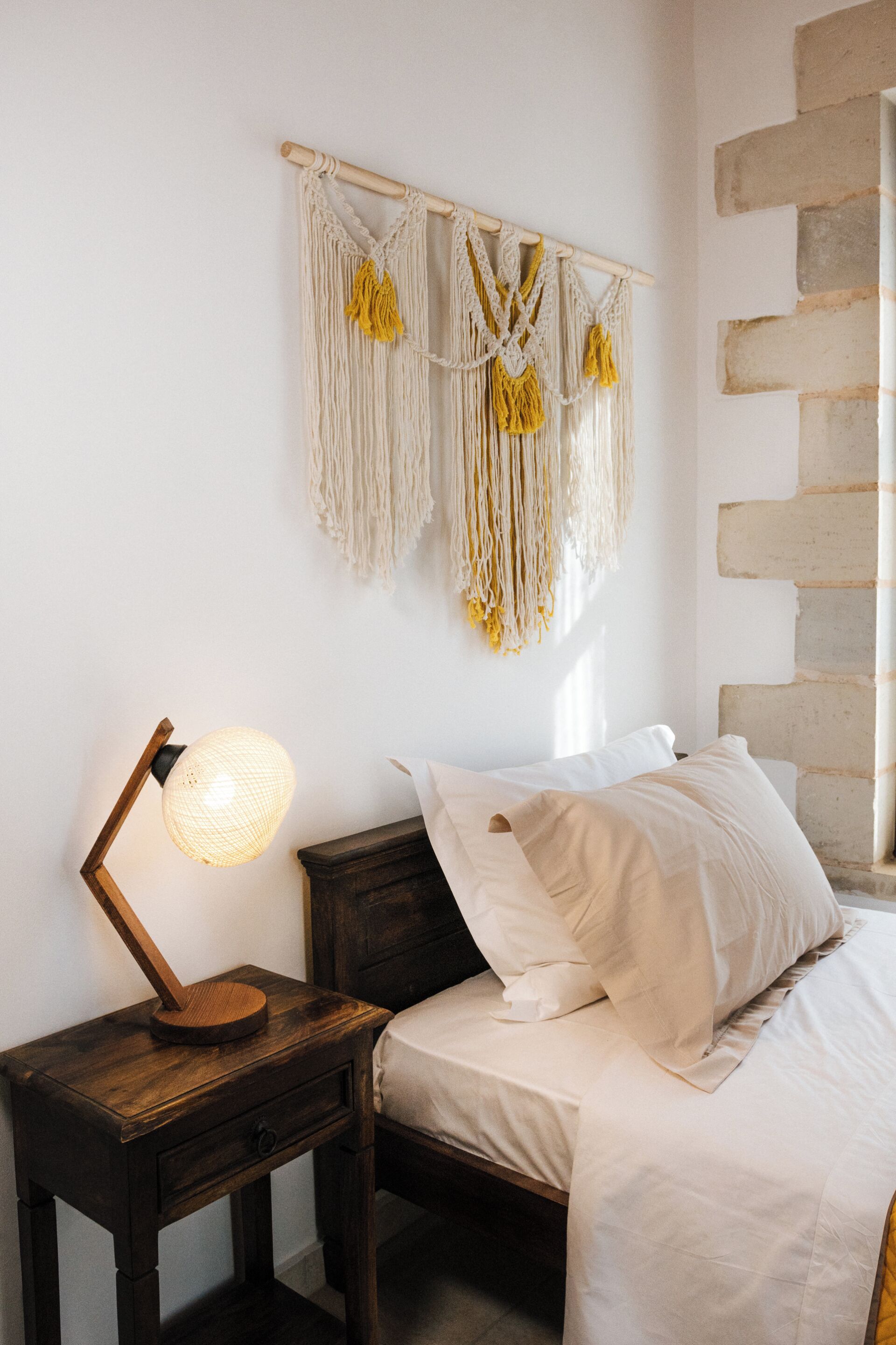 Une chambre à coucher avec un lit, une table de chevet avec une lampe et une décoration murale en macramé.