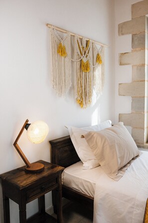 Een slaapkamer met een bed, een nachtkastje met een lamp en een macramé wanddecoratie.