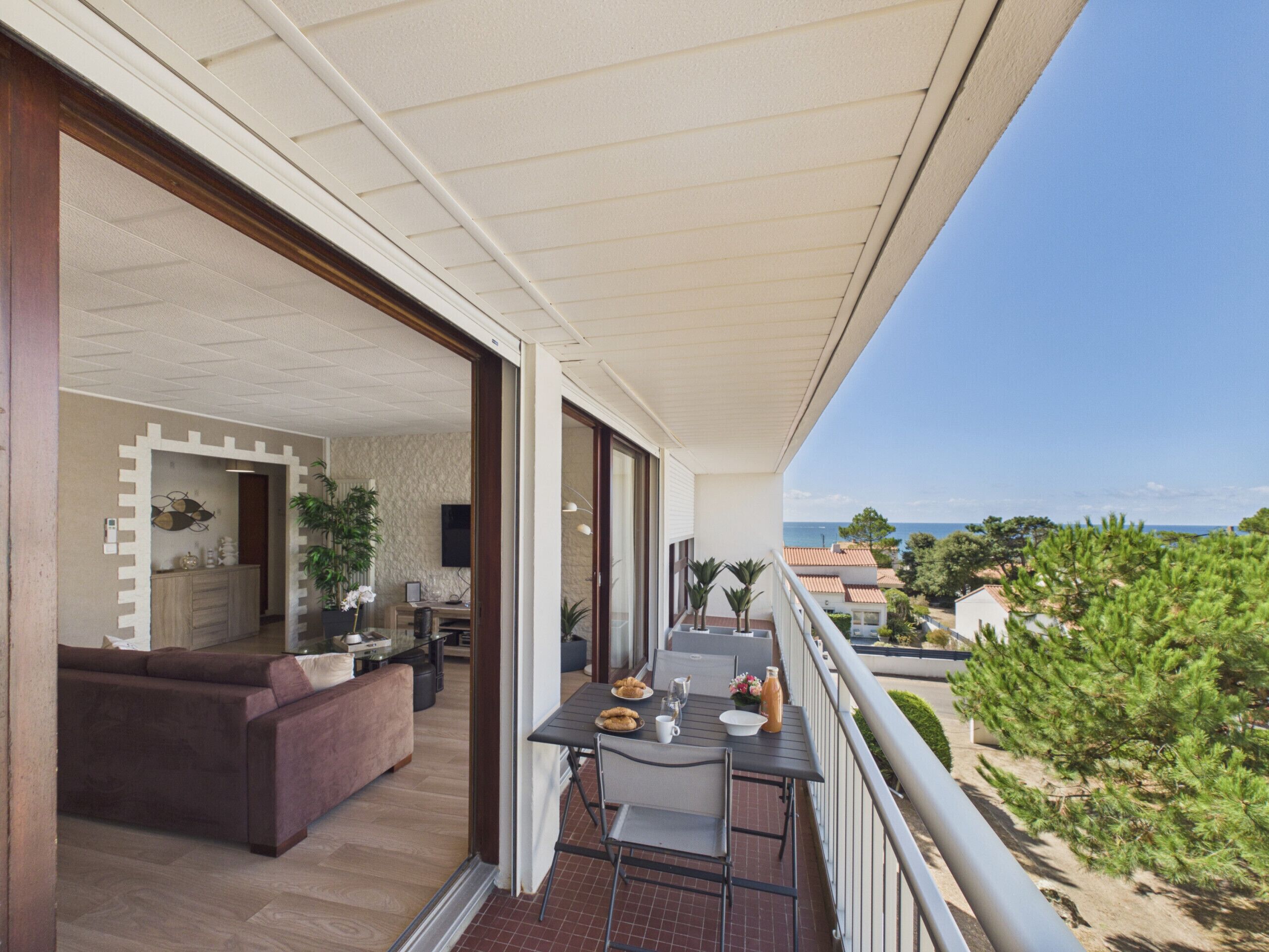 A balcony with a dining table, chairs, and a view of the sea.