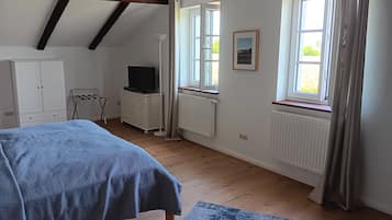 Ein Schlafzimmer mit einem Bett, einem Schminktisch, einem Fernseher und zwei mit Vorhängen versehenen Fenstern.